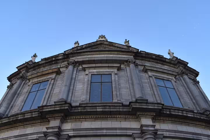Ornate neoclassical building dome with statues and large windows against blue sky in Madrid