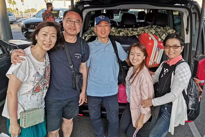 Group of happy tourists posing by a car during a scenic private transfer from Madrid to Lisbon with luggage in the trunk.