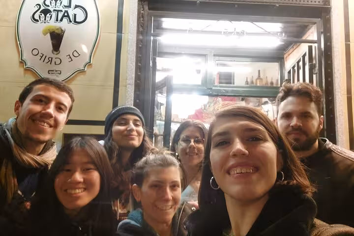 Group of seven friends smiling outside Los Gatos bar in Madrid at night during ghost walking tour
