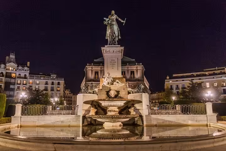 Illuminated monument fountain in Madrid plaza at night with historic buildings in background