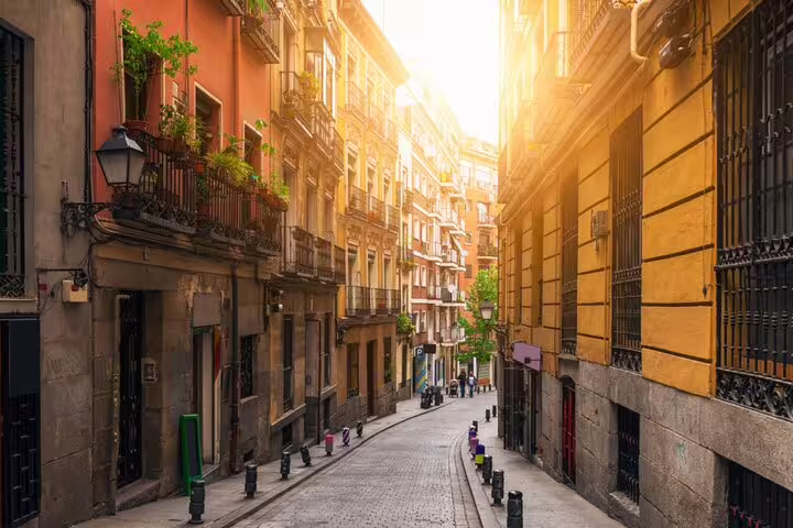 Narrow cobblestone street in Madrid with ornate balconies and warm golden sunlight at sunset