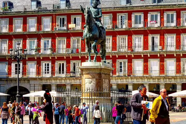 Equestrian statue at Plaza Mayor Madrid with red historic building and tourists