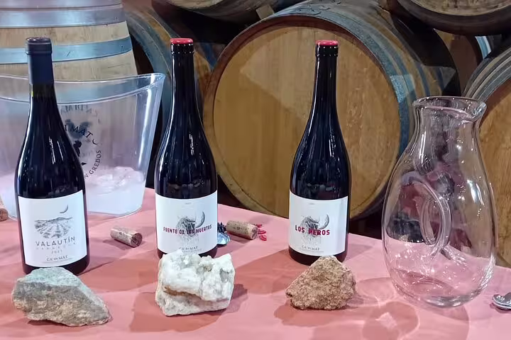 Three bottles of premium Madrid wine displayed with corks and rocks, set against wooden wine barrels in a winery.