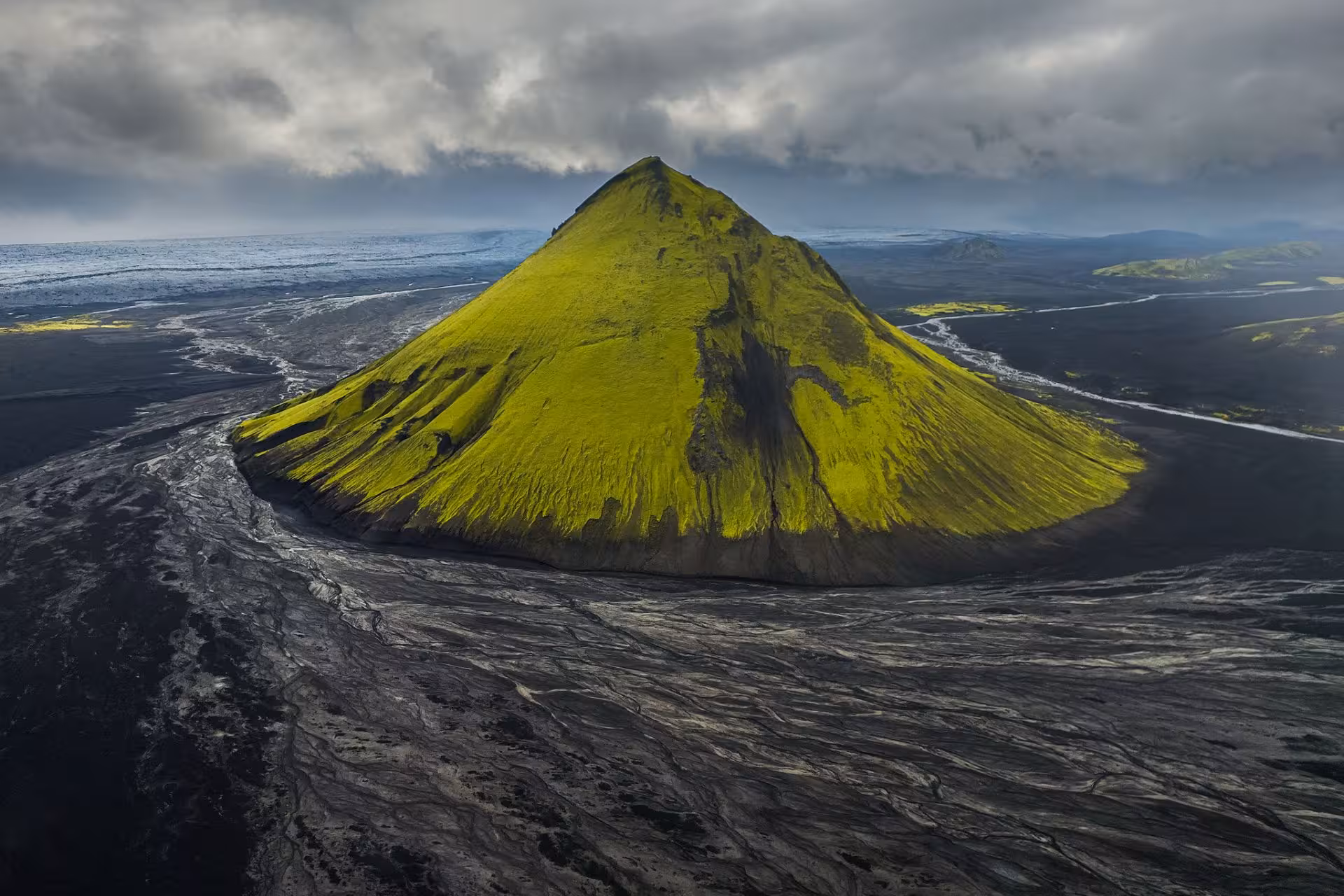 Aerial view of Mælifell volcano covered in bright green moss surrounded by black lava fields in Fjallabak Iceland