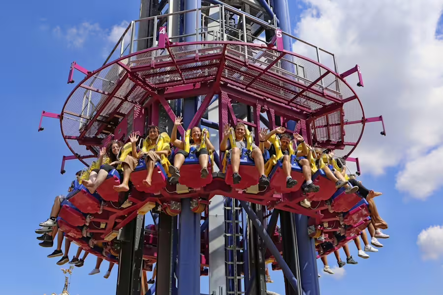 MagicLand Amusement Park drop tower ride with seated riders, adrenaline attraction with blue sky backdrop