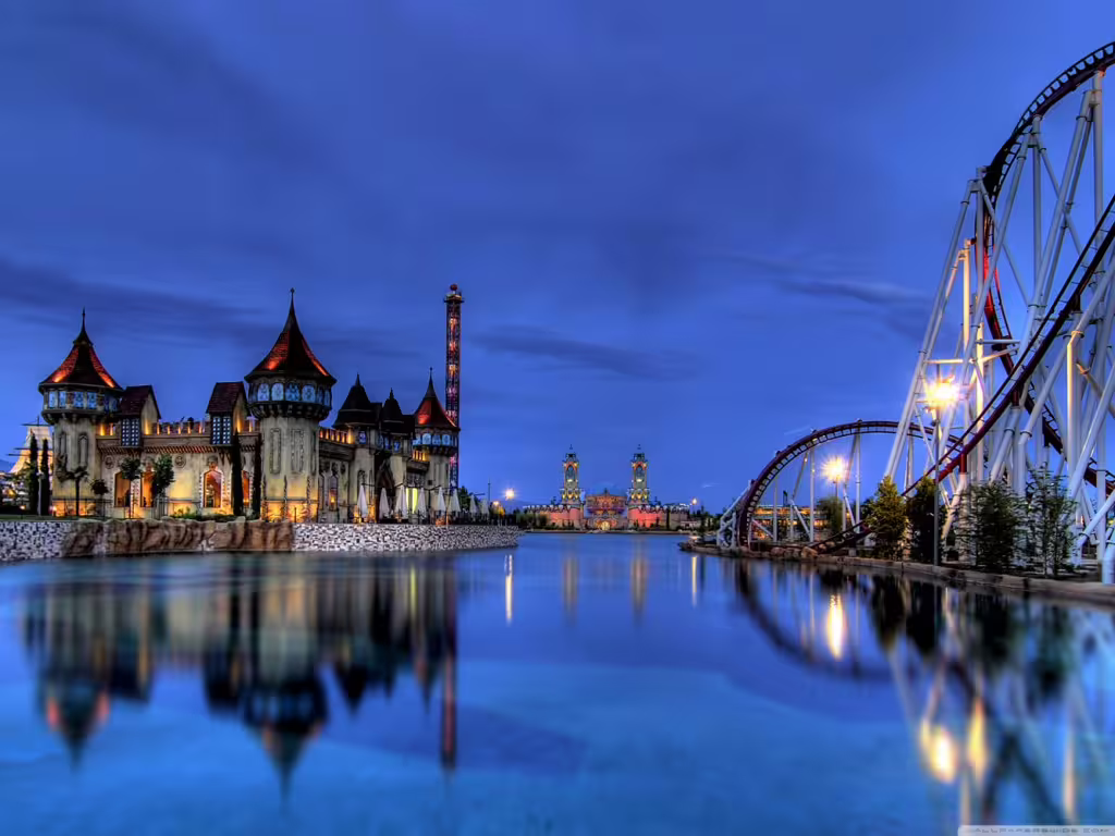 MagicLand Amusement Park night skyline with illuminated castle and roller coaster by the lake, entrance ticket tour