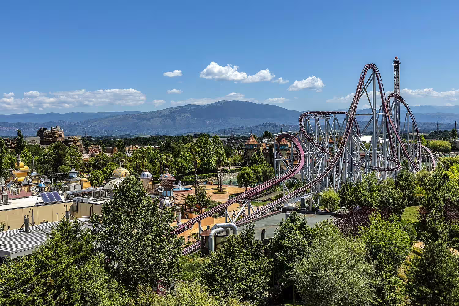 Panoramic view of MagicLand amusement park roller coaster with looping track and mountain backdrop
