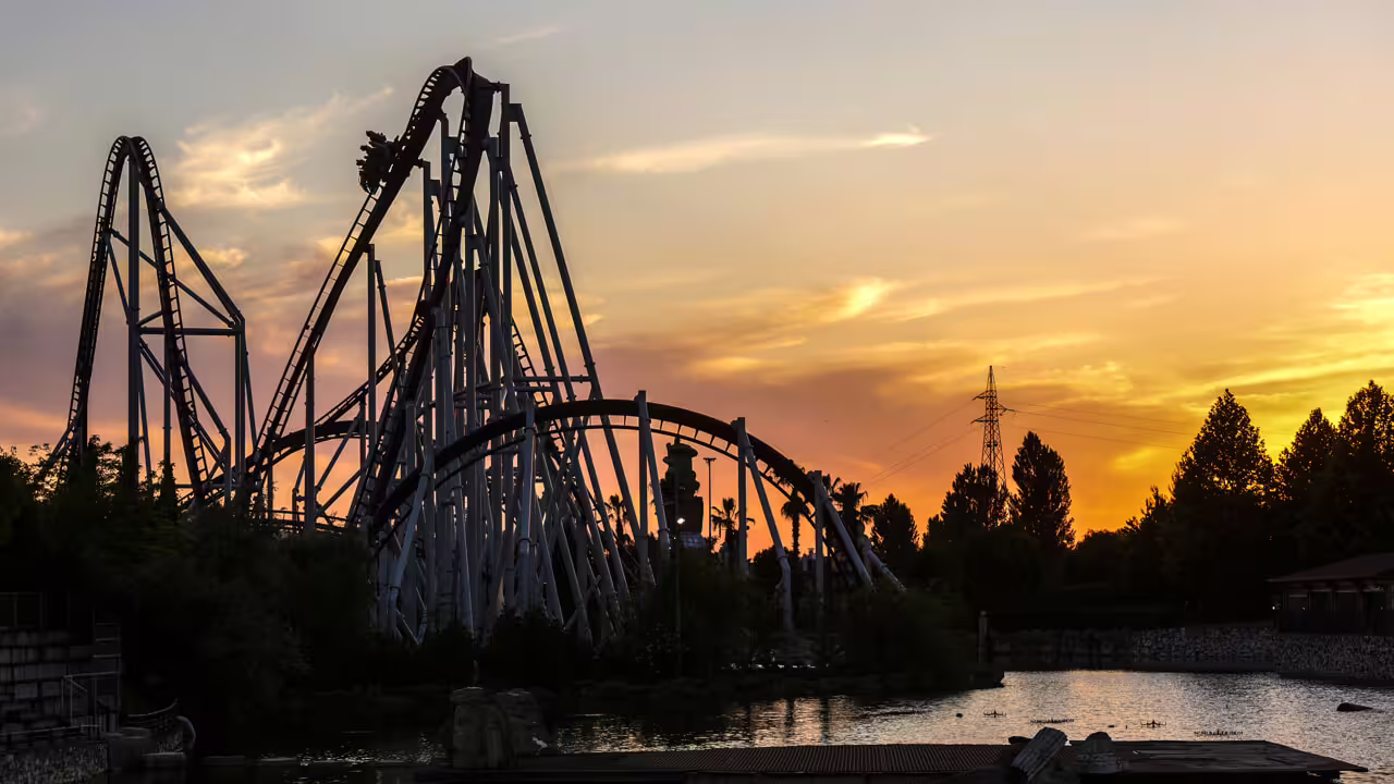 MagicLand Amusement Park roller coaster silhouette at sunset over the lake, thrill ride view with entry ticket