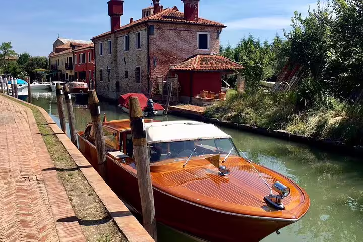 Mahogany boat docked beside charming Venetian buildings on a serene canal, showcasing a classic Italian scene.
