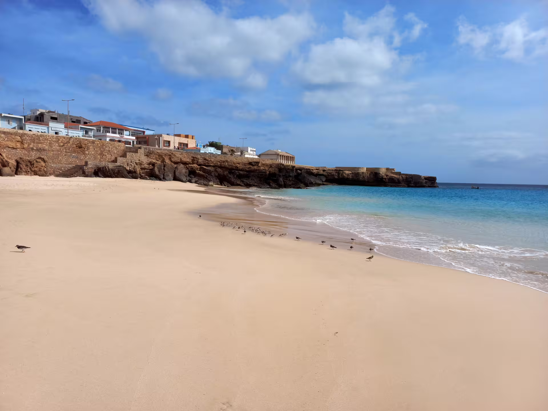 Scenic view of a serene beach with birds and coastal village on Maio Island, ideal for a relaxing island tour.