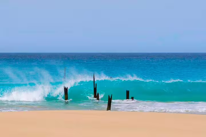 Tranquil beach scene on Maio Island with turquoise waves crashing against old wooden posts on a sandy shore.