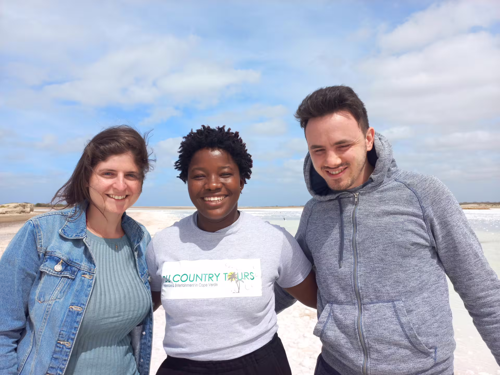 Group of happy tourists posing together at the scenic salt flats on Maio Island during a guided tour.