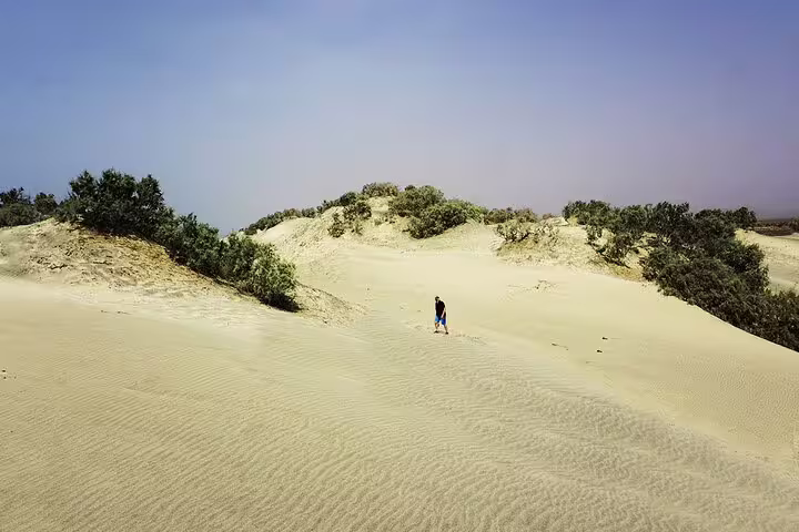 Traveler explores the sandy dunes of Maio Island under a clear blue sky, highlighting the unique landscape of Cape Verde.