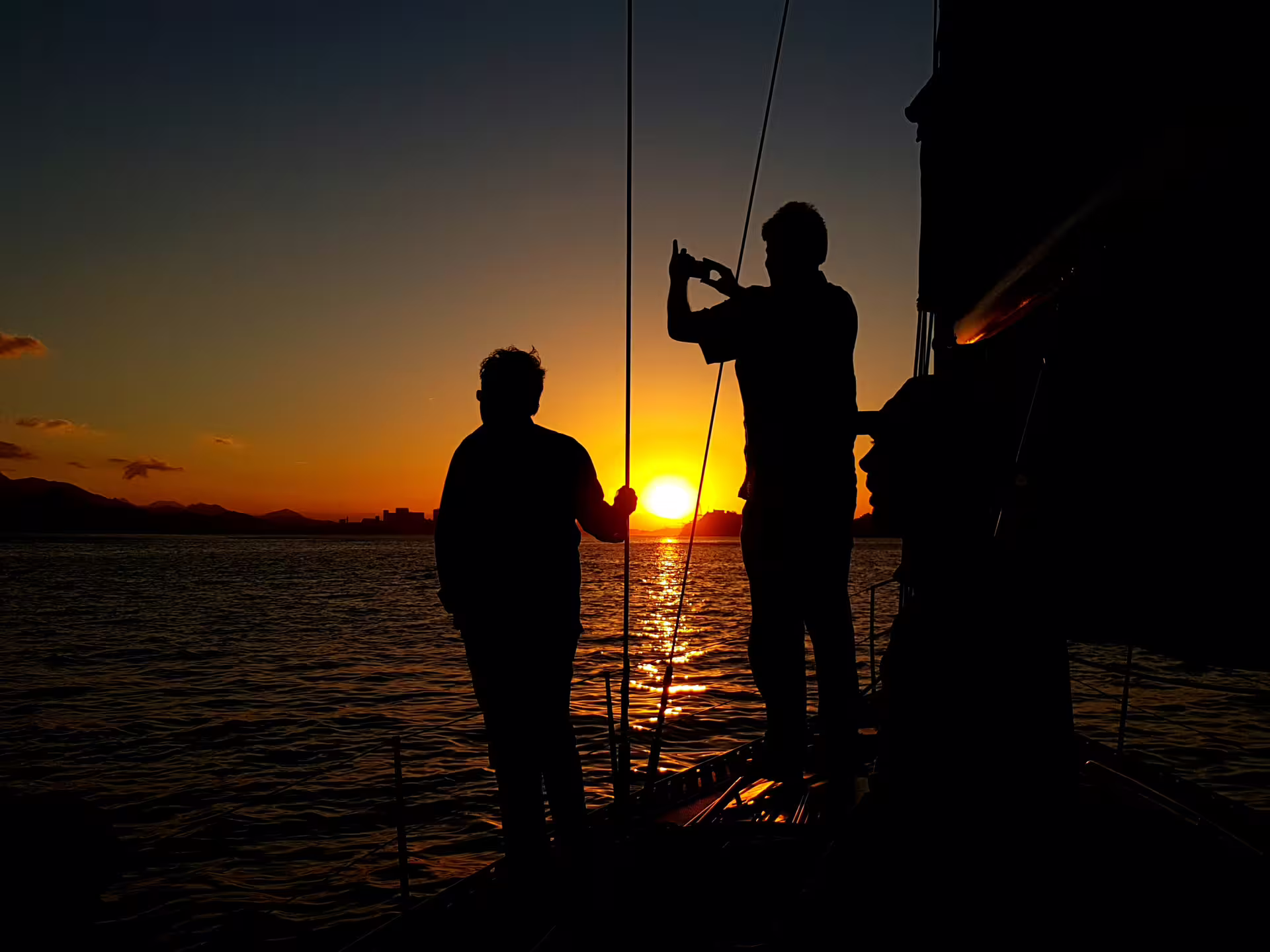 Silhouetted figures enjoy a breathtaking sunset on a private sailing tour aboard the MAKANI MAIKAI.