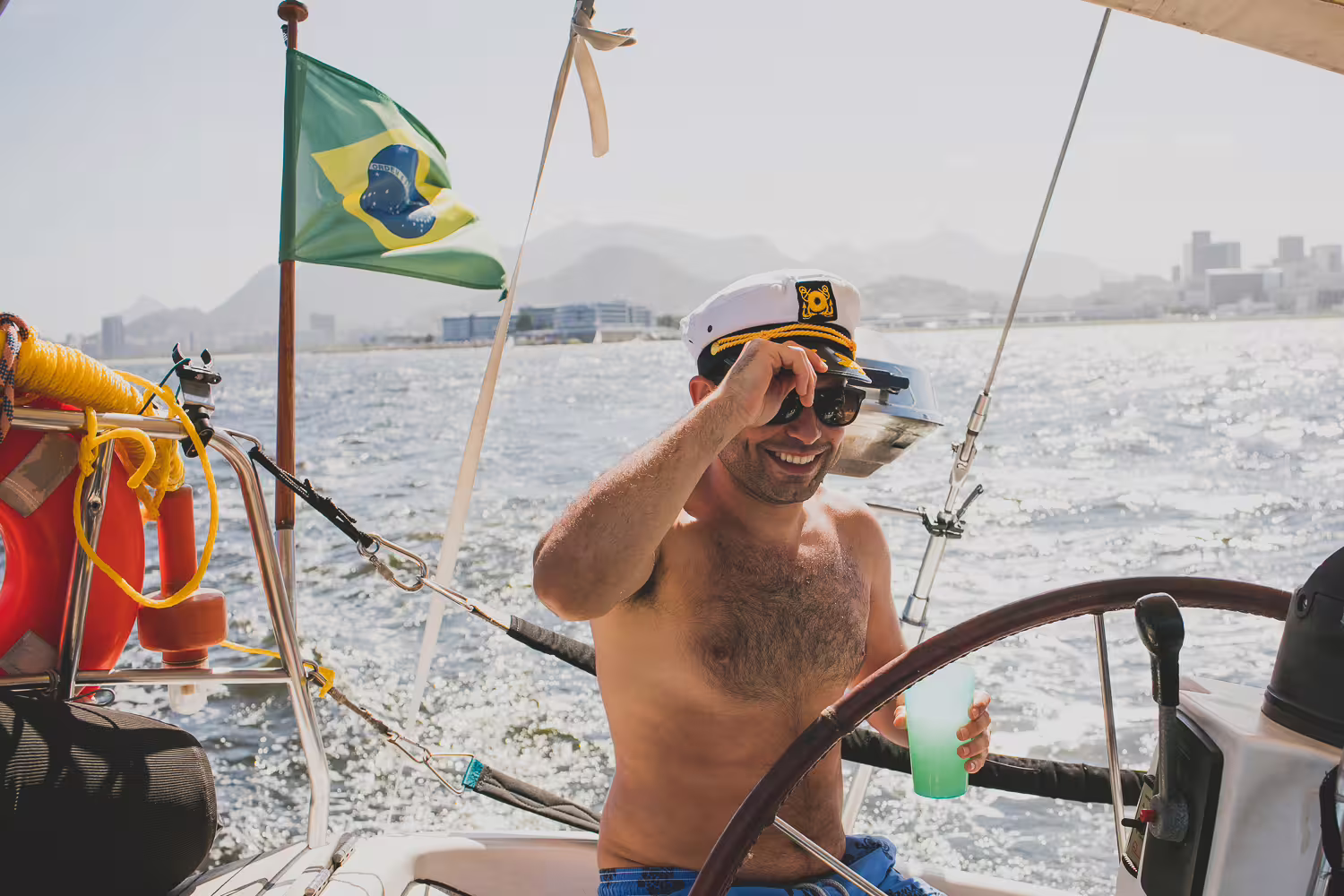 Smiling captain enjoying a sunny day steering the MAKANI MAIKAI private sailing tour with Brazilian flag waving.