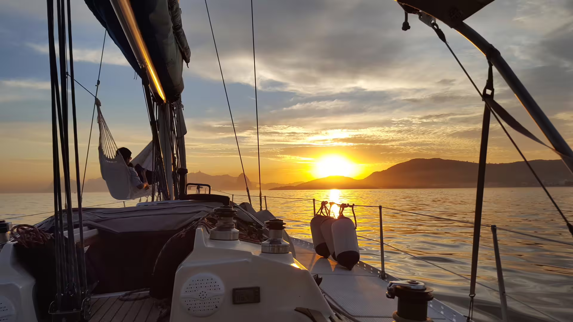 Experience a breathtaking sunset aboard Makani Maikai, featuring tranquil seas and a relaxing hammock view.