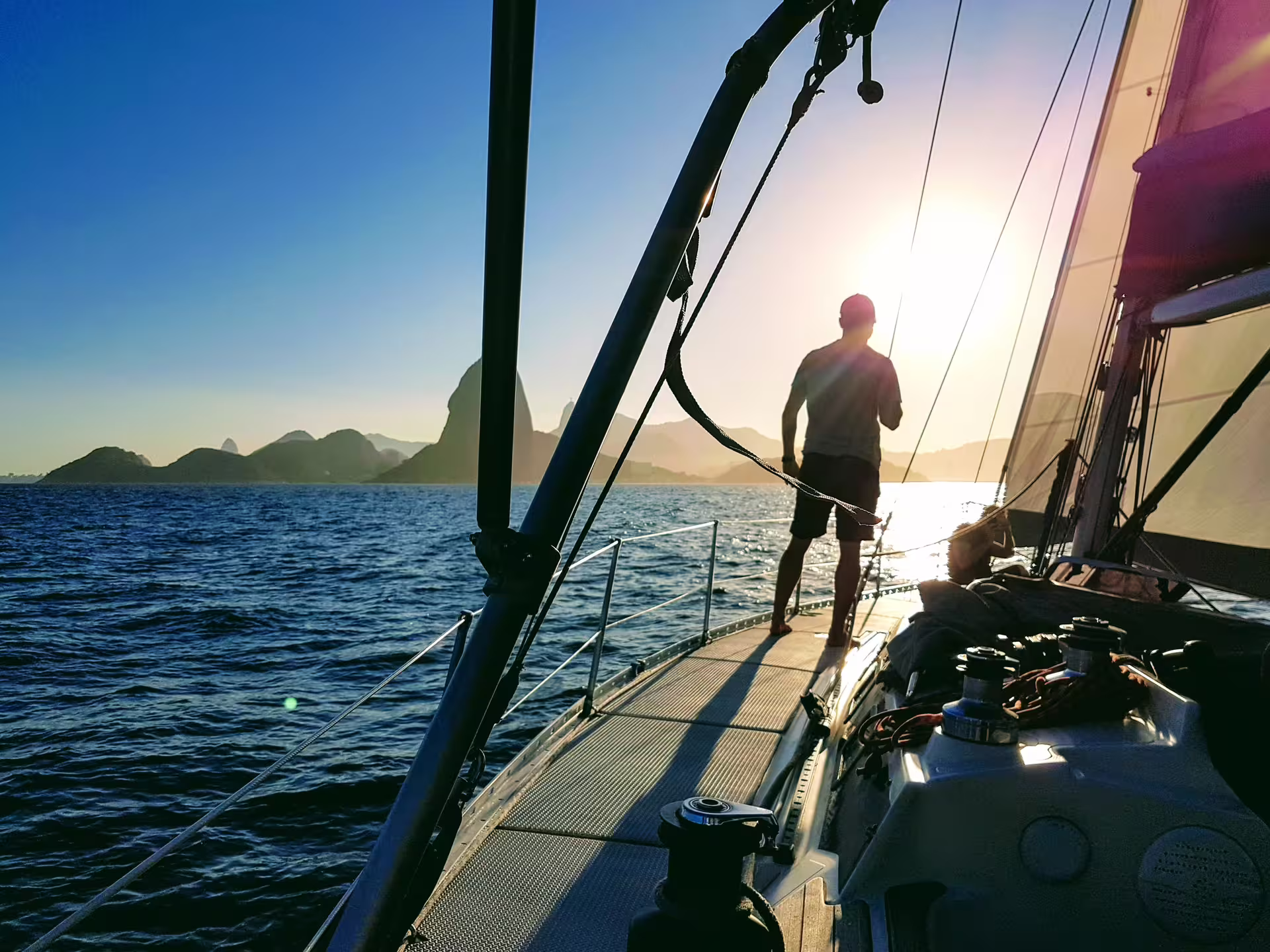 Man stands on the deck of the MAKANI MAIKAI yacht with stunning ocean views and distant mountains.