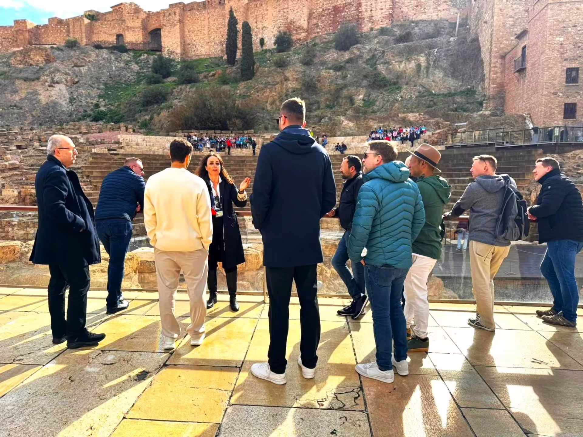 Local guide leading a Malaga group walking tour at the Roman Theatre with Alcazaba fortress walls behind