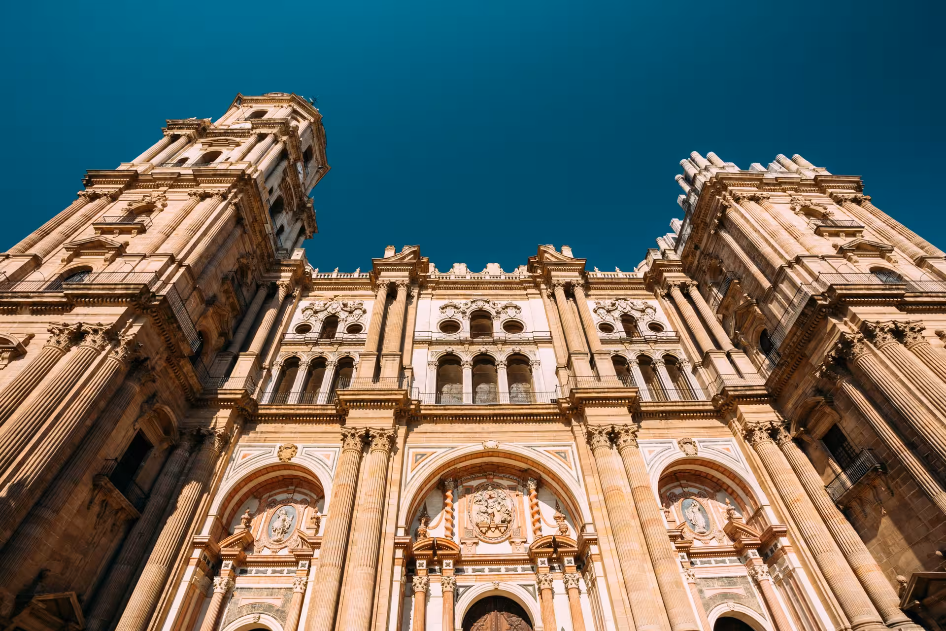 Impressive facade of Malaga Cathedral featuring ornate carvings and grand arches against a clear sky backdrop.