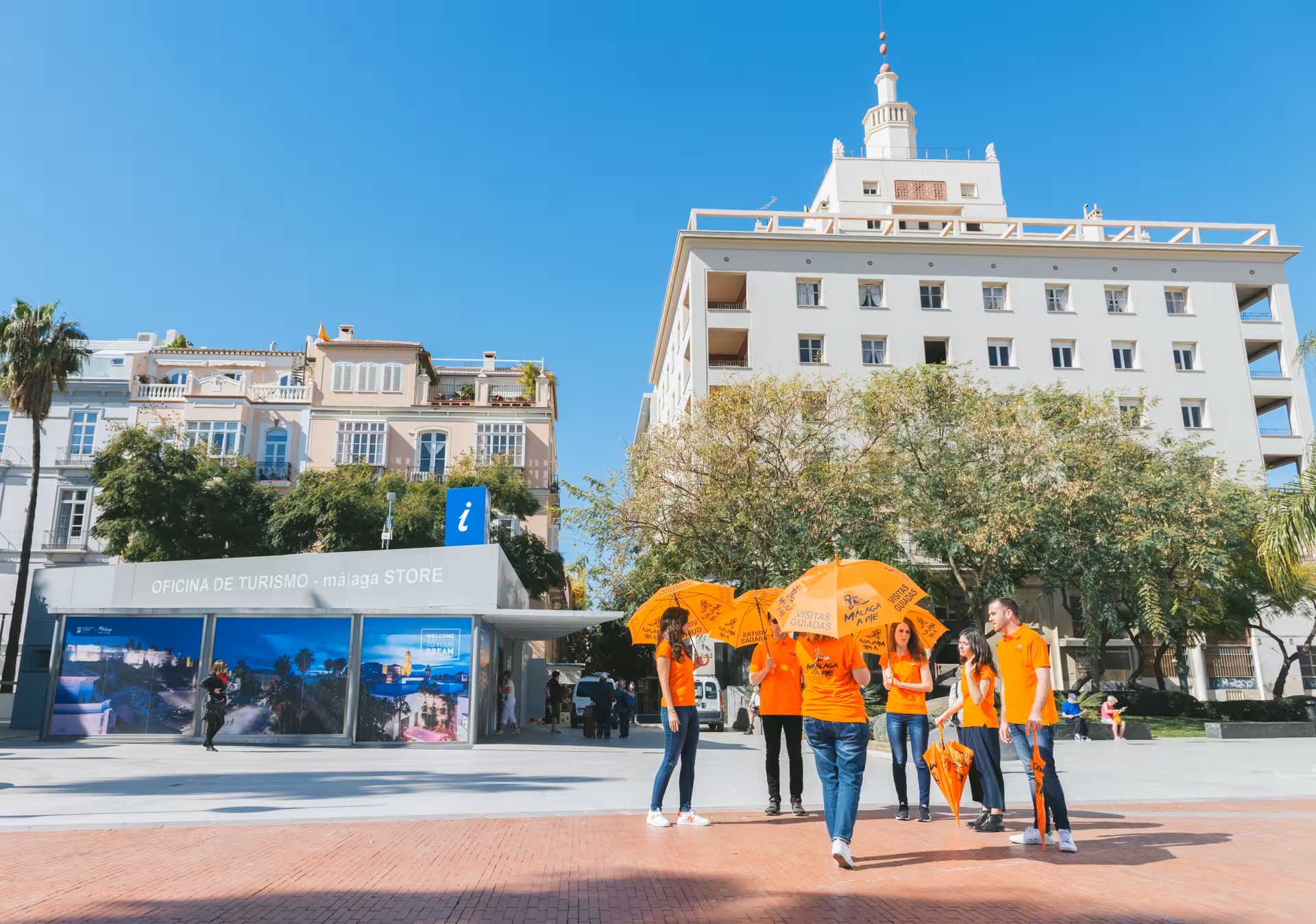 Tourists gather at Malaga Tourism Office, starting point for guided tours with Alcazaba, Theater, and Cathedral visits.