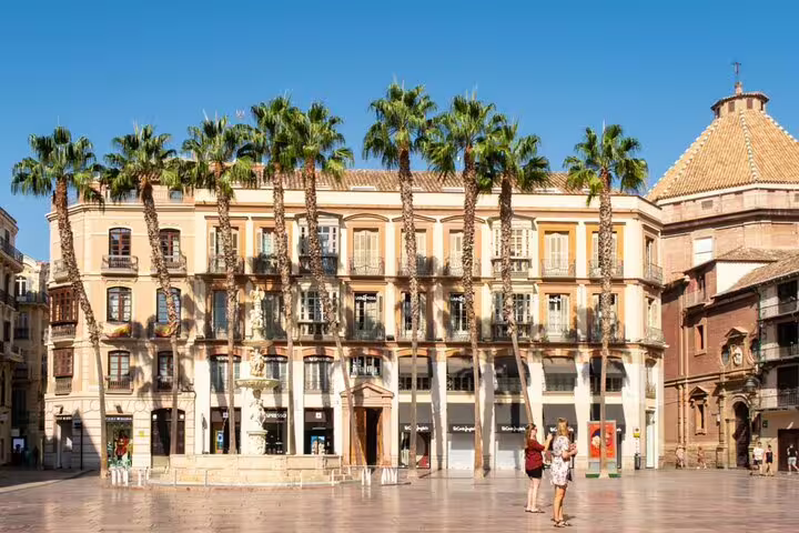 Plaza de la Constitución in Málaga with palm trees, historic buildings, and a central fountain on a sunny day