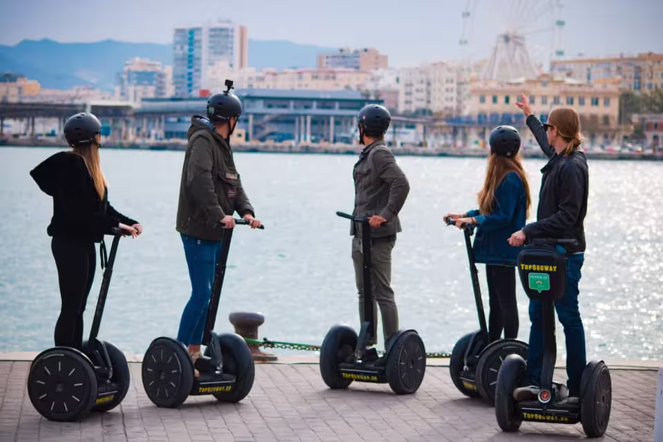 Group enjoying panoramic Segway tour along Malaga waterfront with cityscape views in the background.