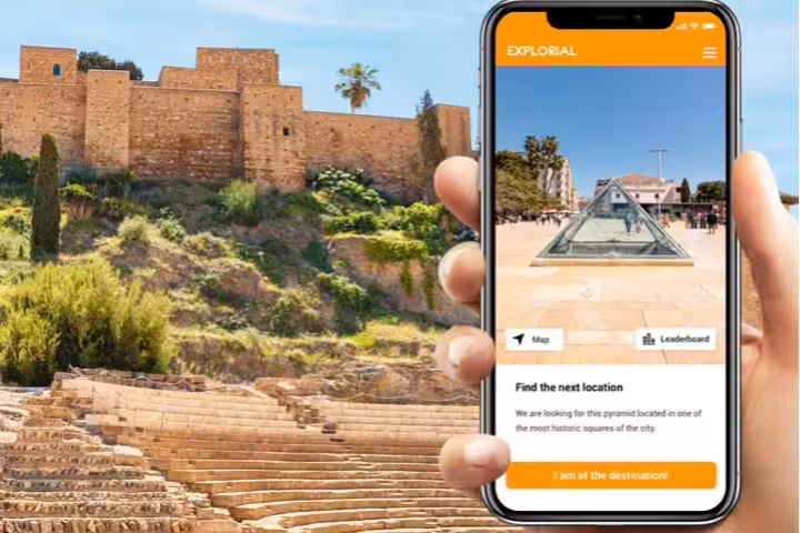 Phone app guiding Malaga scavenger hunt tour with Alcazaba fortress and Roman theatre in the background