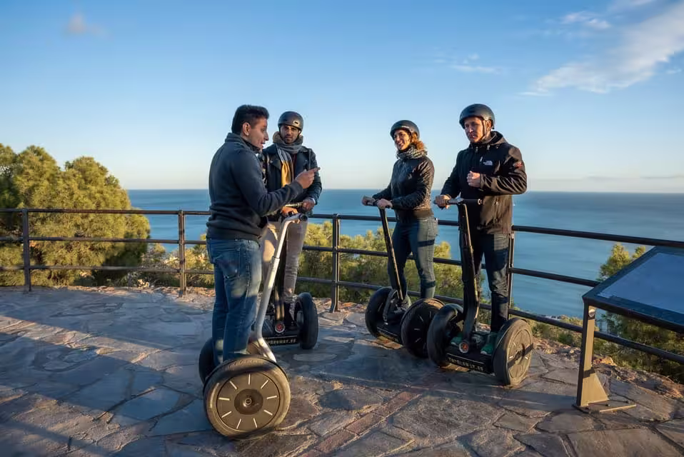 Group of tourists on Segways listening to a guide with a stunning ocean backdrop in Malaga.