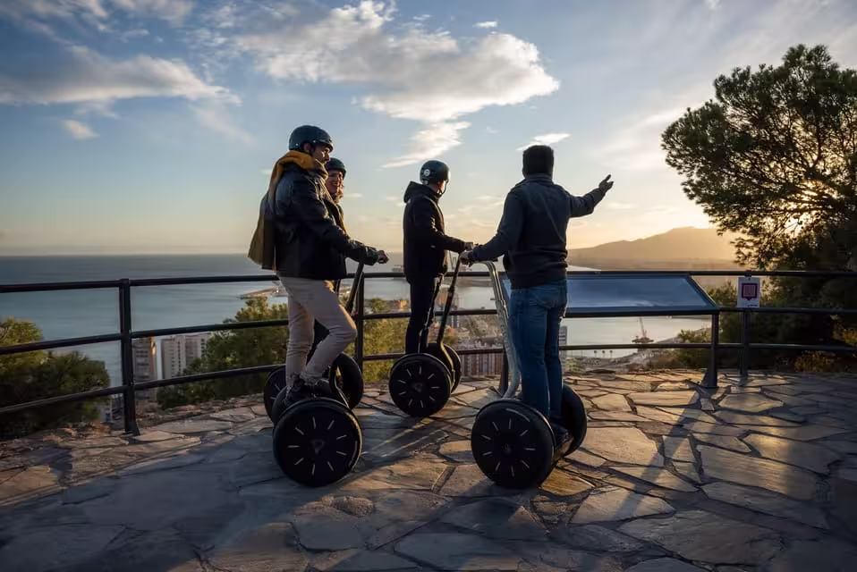 Tourists enjoy a scenic sunset view of Malaga on a Segway tour, overlooking the ocean and city skyline.