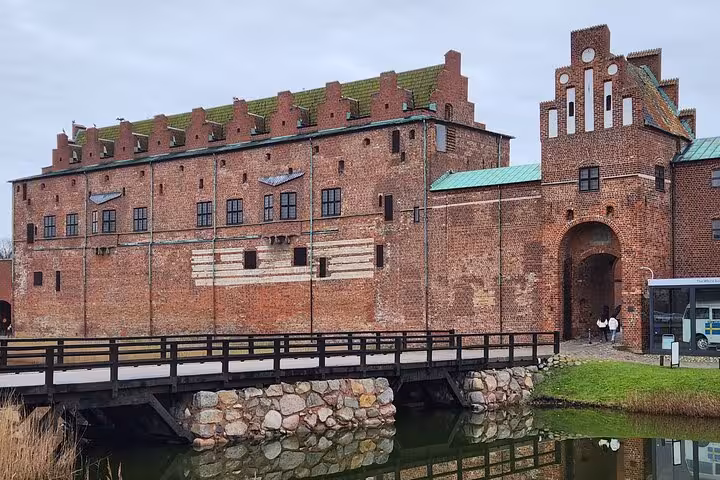Stunning view of Malmö Castle's red brick walls, complete with a wooden bridge and reflective moat.