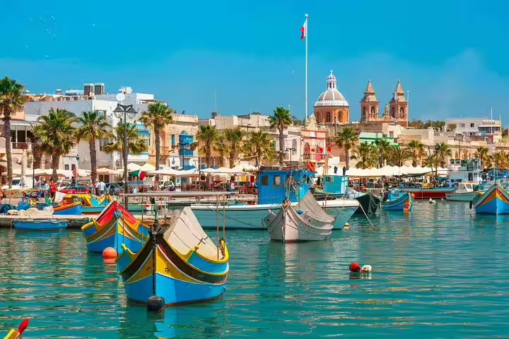 Colorful traditional Maltese boats in a vibrant harbor with historical architecture, perfect for a full-day sightseeing ride.