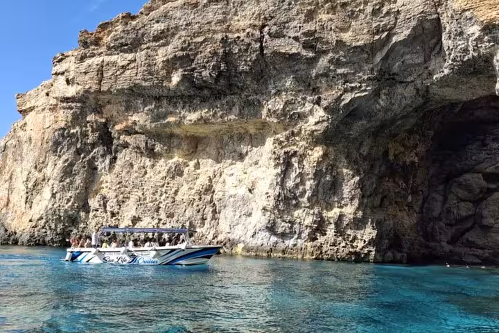 Boat cruising past Gozo sea caves on Half Day Malta tour to Comino Blue Lagoon, crystal-clear water views