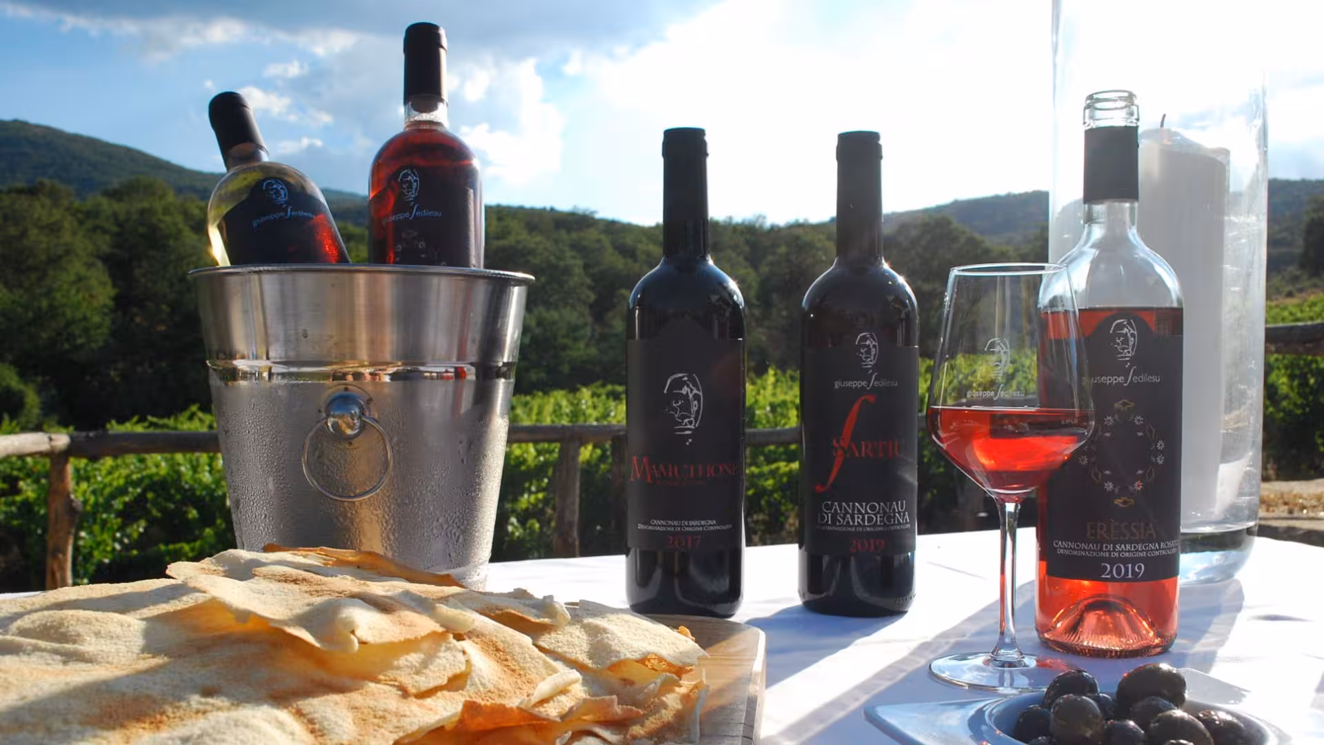 Selection of Mamoiada wines with traditional Sardinian bread, set against a scenic vineyard backdrop.