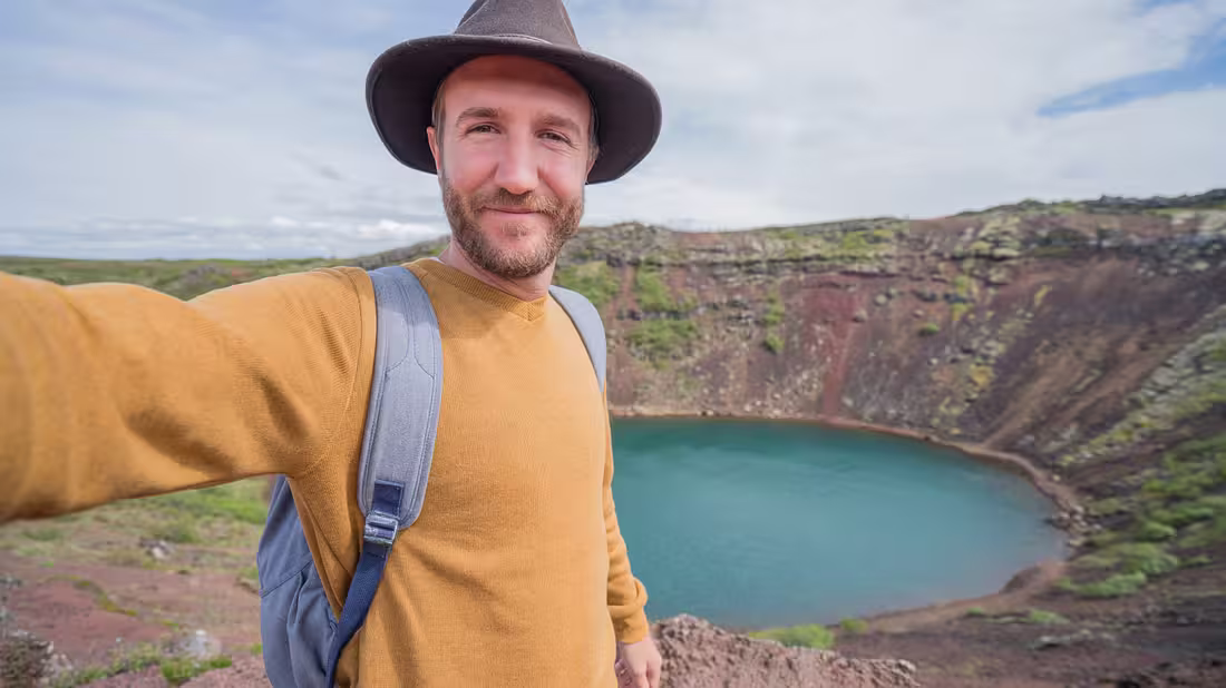 Man standing holding a camera at Kerið crater lake, with the crater lake in the background