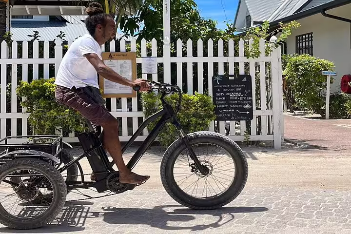 Man cycling on a tricycle through La Digue, Seychelles, showcasing eco-friendly transport on Praslin & La Digue tour.