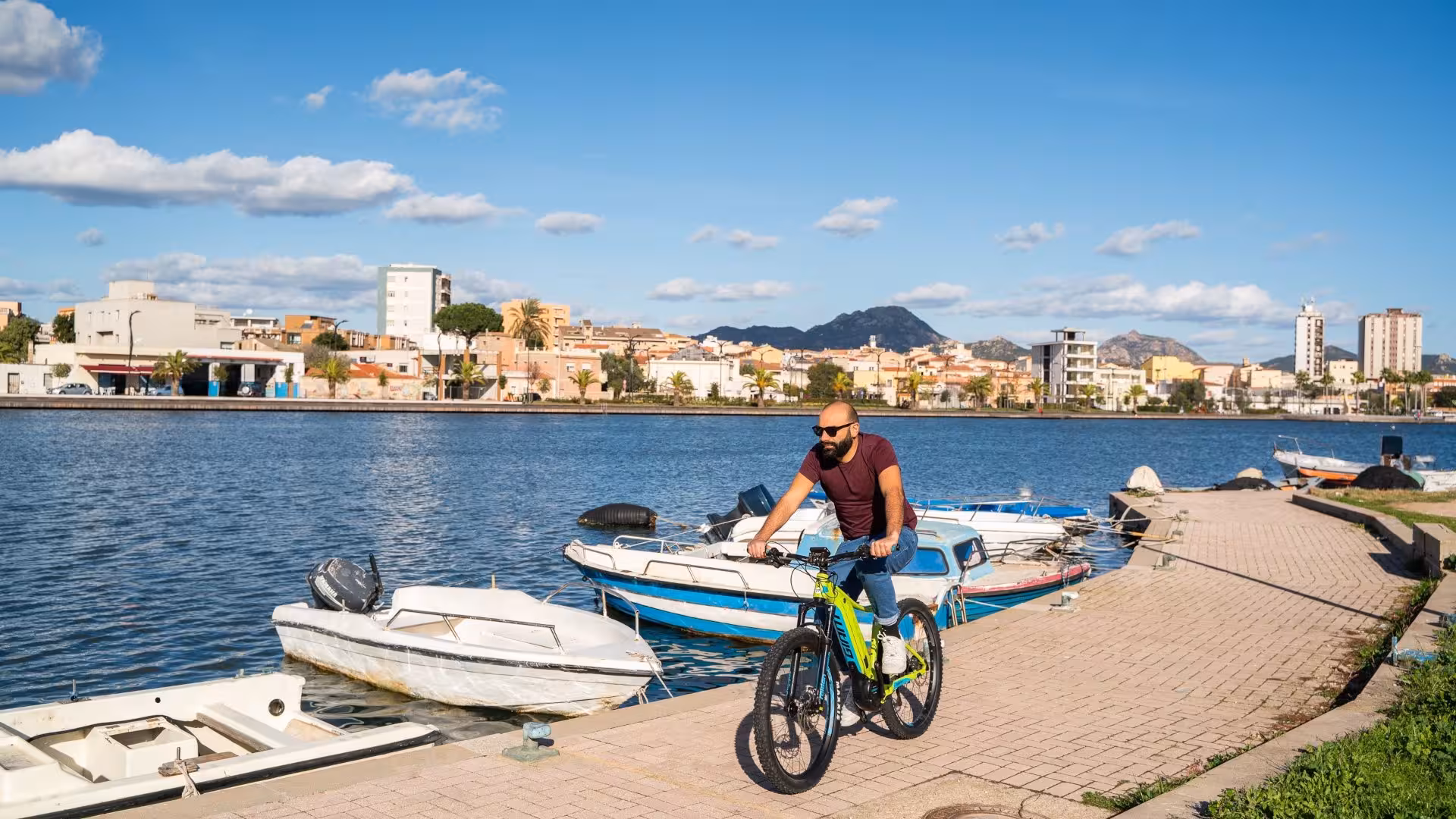Man riding an e-bike along Olbia's waterfront in Sardinia, enjoying a sunny day by the harbor.
