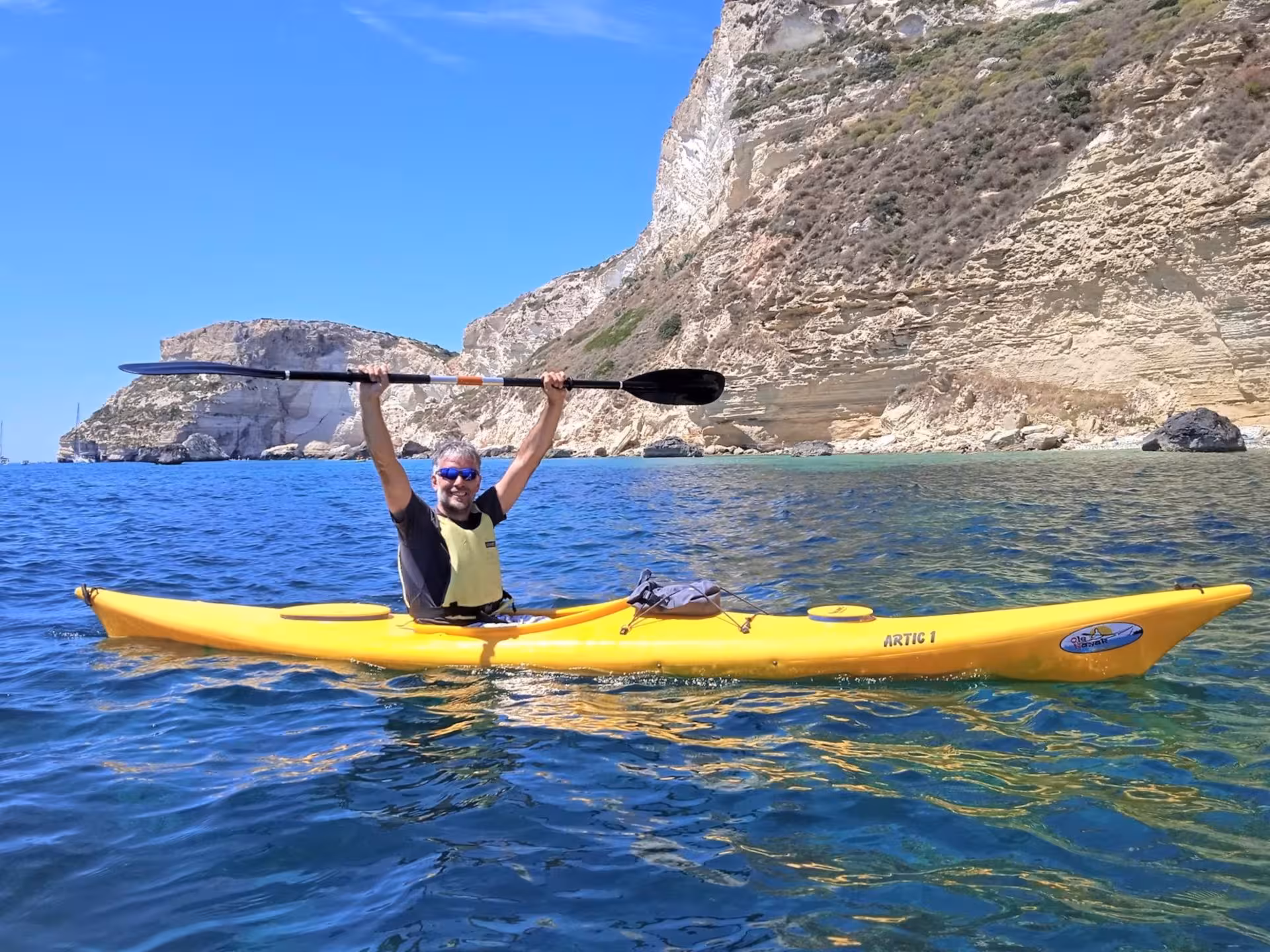 Man enjoys a vibrant kayak excursion along Cagliari's stunning rocky coastline under a clear blue sky.