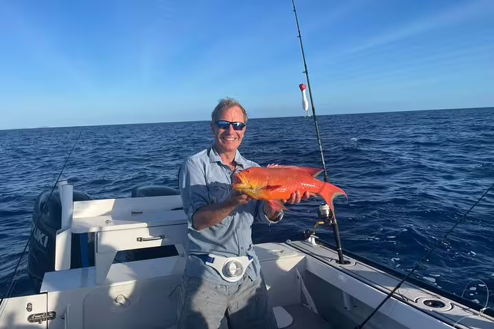 Man holds vibrant orange fish on a Seychelles fishing boat under clear blue skies.