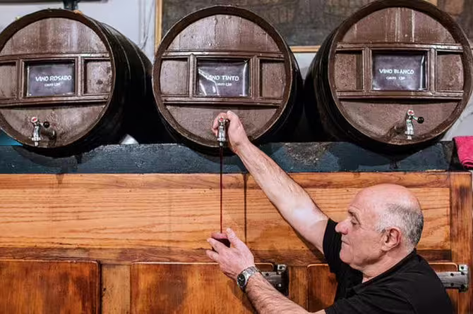 Man pouring wine from wooden barrels, showcasing traditional wine-tasting experience.