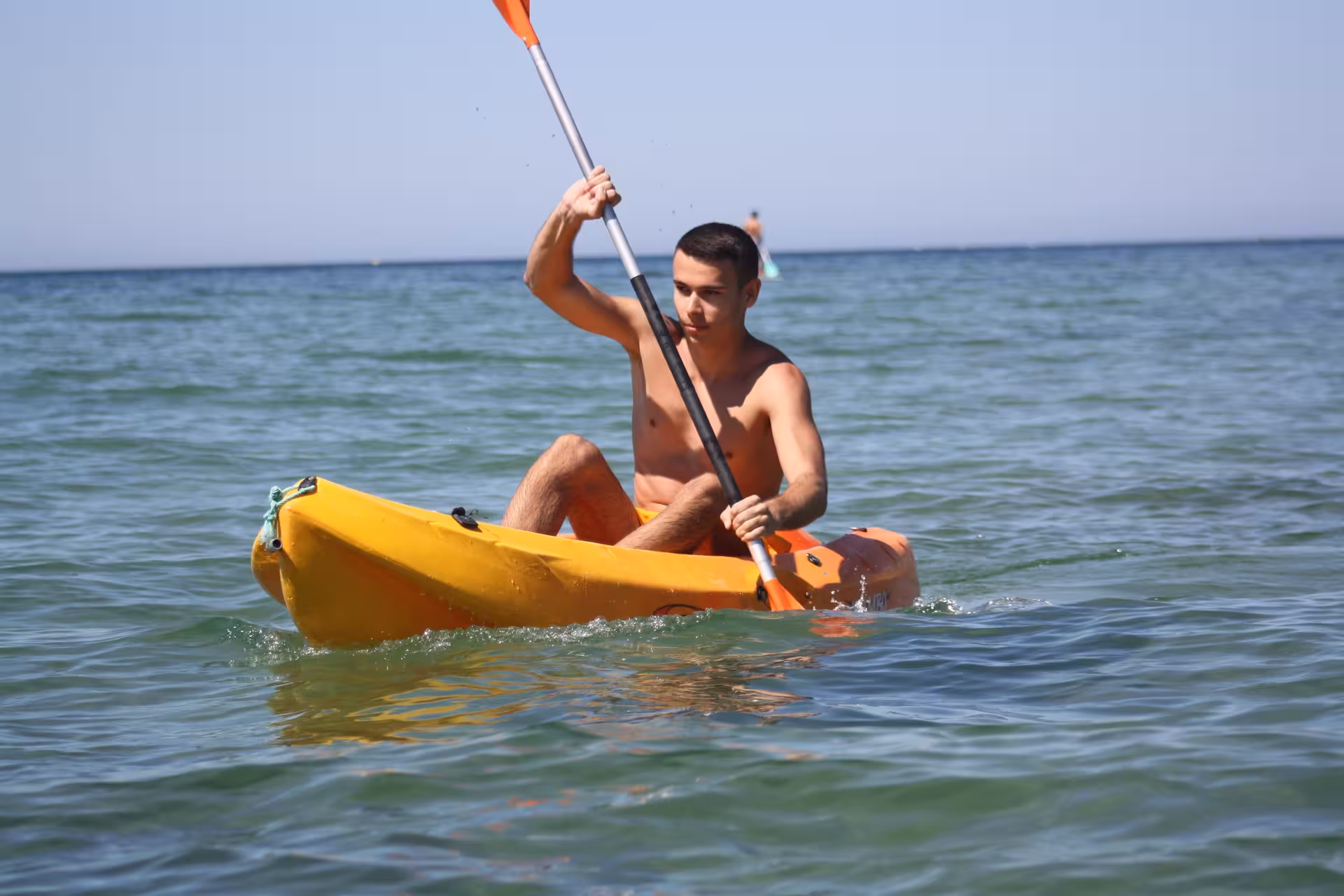 Young man kayaking solo in a bright yellow kayak on clear open ocean waters on a sunny day