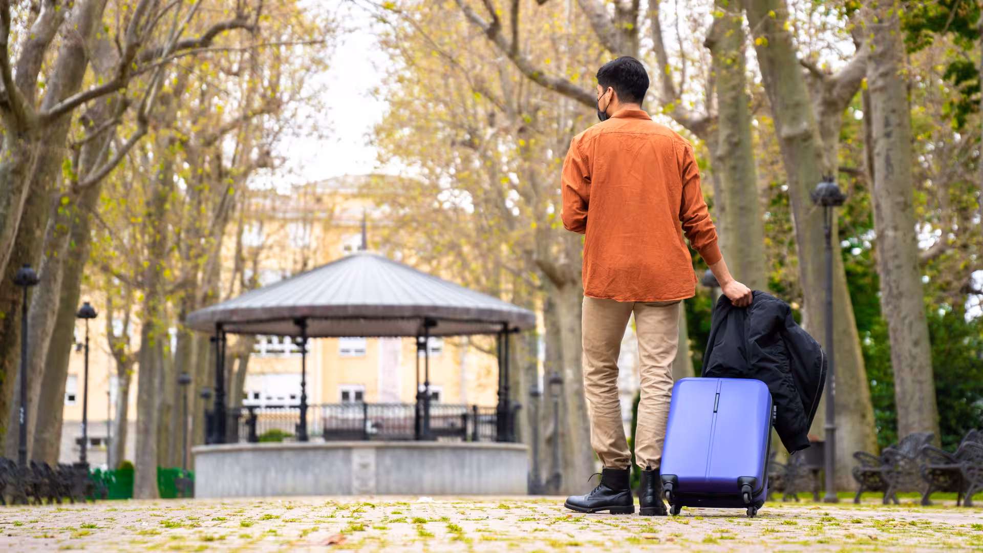 Man with rolling suitcase in park, book secure London luggage storage in Paddington for stress-free travel