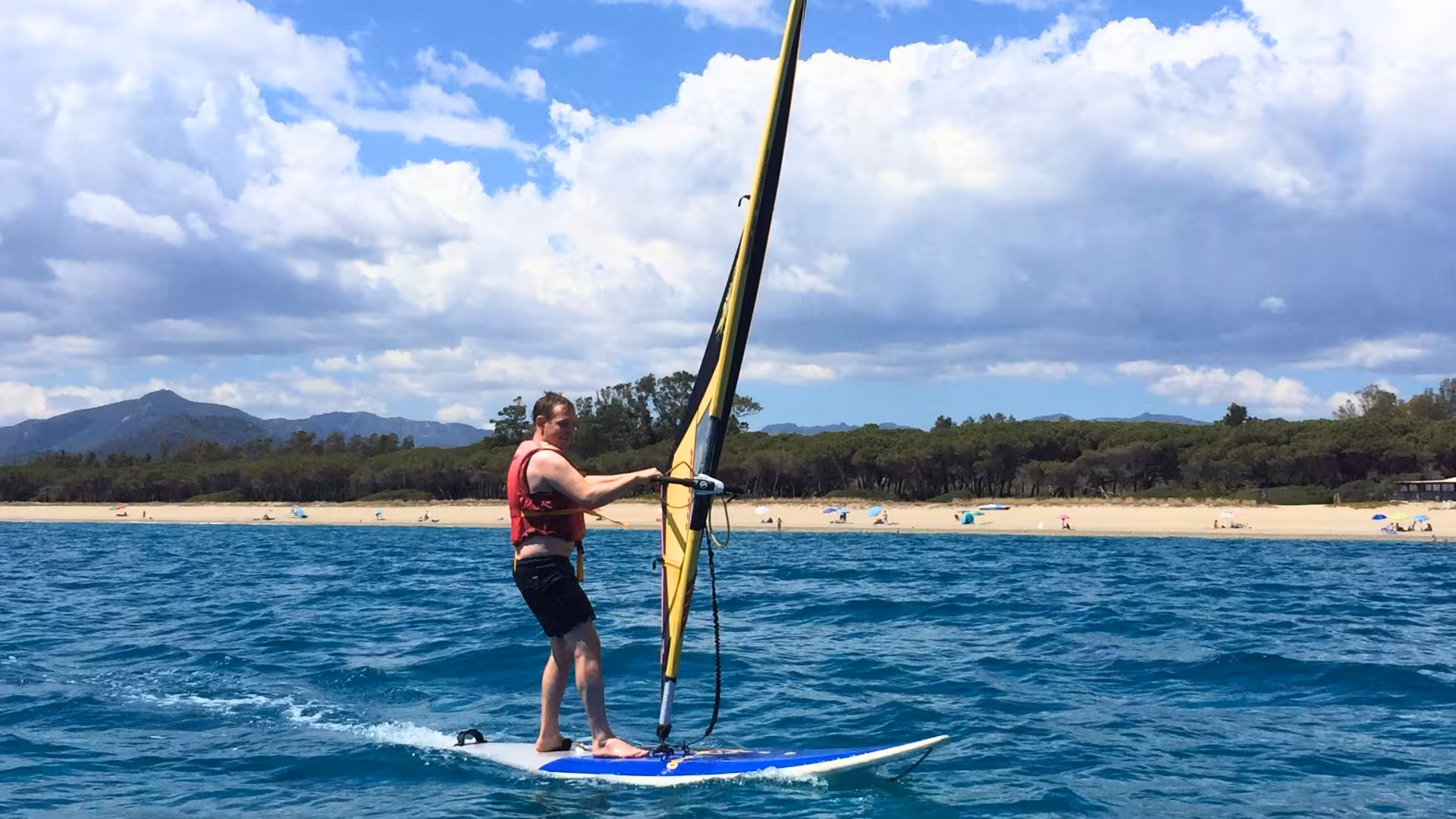 Man windsurfing near Bari Sardo's sandy shores, showcasing the vibrant and accessible windsurfing courses available.
