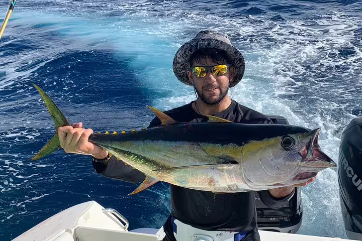 Man holds a large yellowfin tuna aboard a boat during an exhilarating Seychelles fishing adventure.