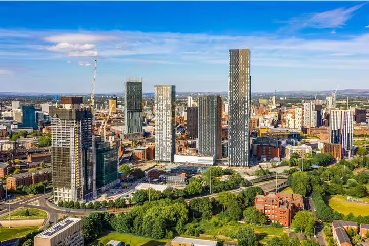 Aerial view of Manchester city centre skyline with modern skyscrapers and green trees on a sunny day