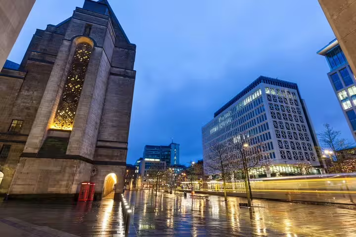 Rainy night in Manchester city centre with illuminated historic building and modern offices reflecting on wet pavement