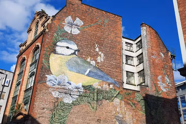 Large street art mural of a blue tit bird with flowers painted on a red brick building in Manchester