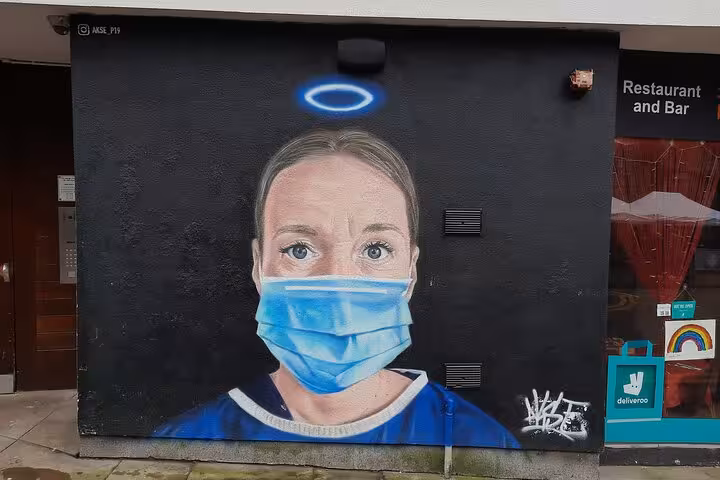Street art mural of NHS nurse wearing blue face mask with angel halo on black wall in Manchester