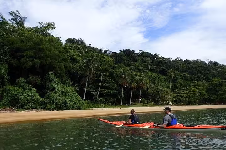 Kayakers glide along the shoreline, enjoying the scenic view of tropical greenery and sandy beaches.