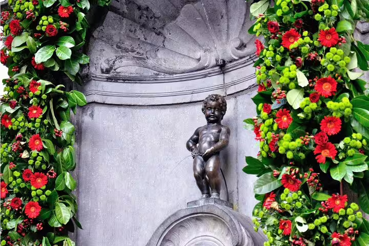 Manneken Pis bronze statue fountain surrounded by red flowers and green foliage in Brussels