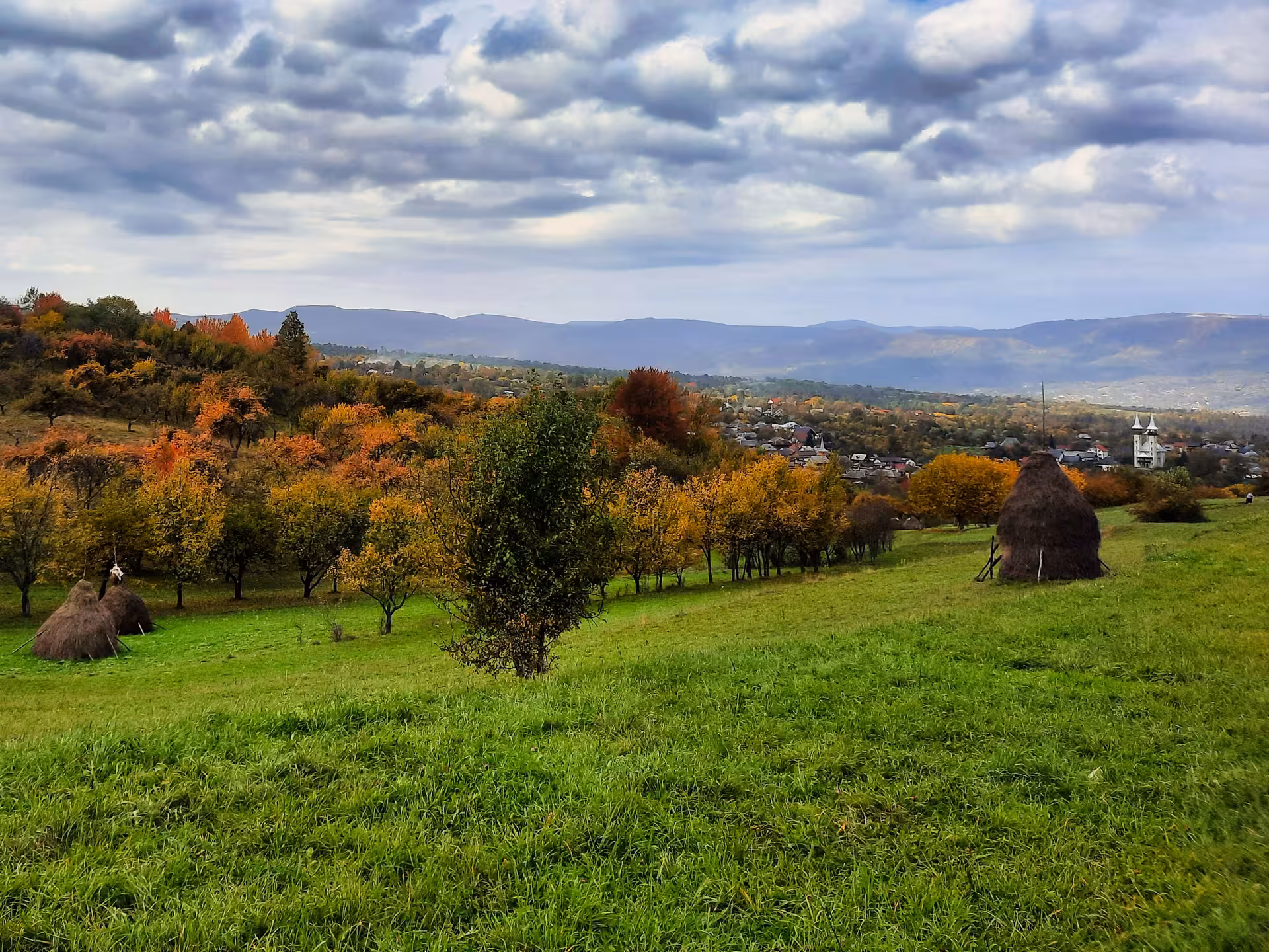 Scenic autumn landscape of a Maramures rural village with haystacks, colorful trees, and misty mountains